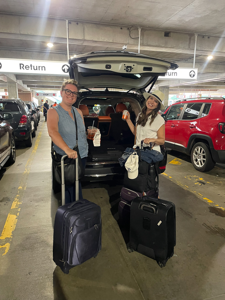 packing carry on only for a girls trip, showing two girls with luggage and a car in a garage